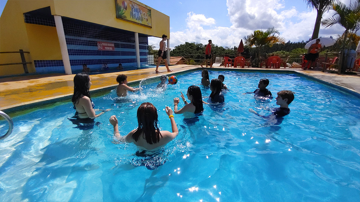 Foto de alunos brincando em piscina ao ar livre, em passeio externo