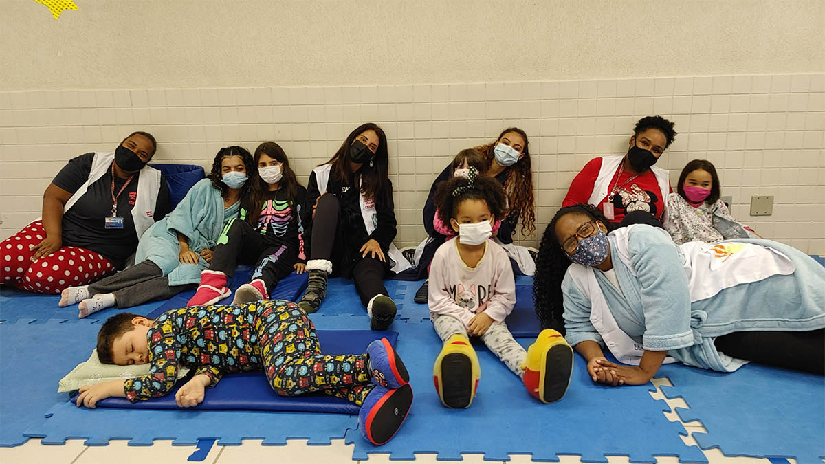 Imagem de alunos e equipe pedagógica em sala sob tapete de EVA posando para foto