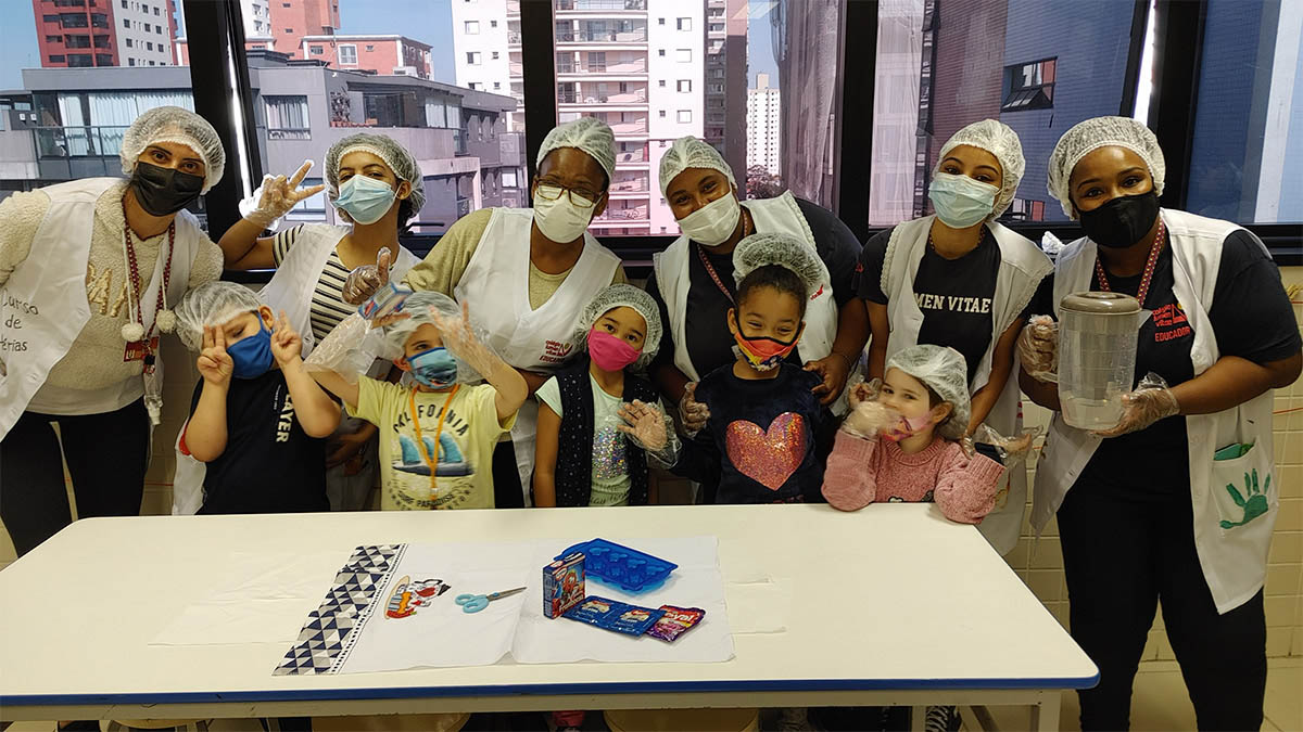 Imagem de alunos e equipe pedagógica em atividade culinária, posando para foto