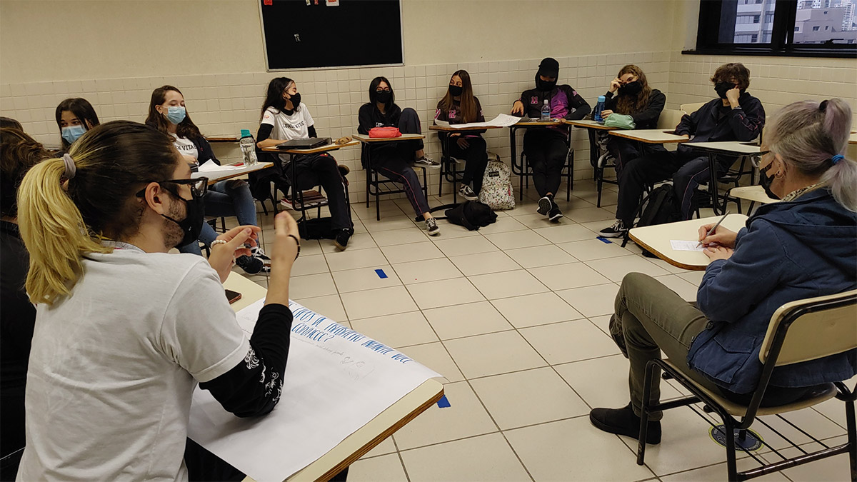 Foto de alunos reunidos em carteiras em círculo