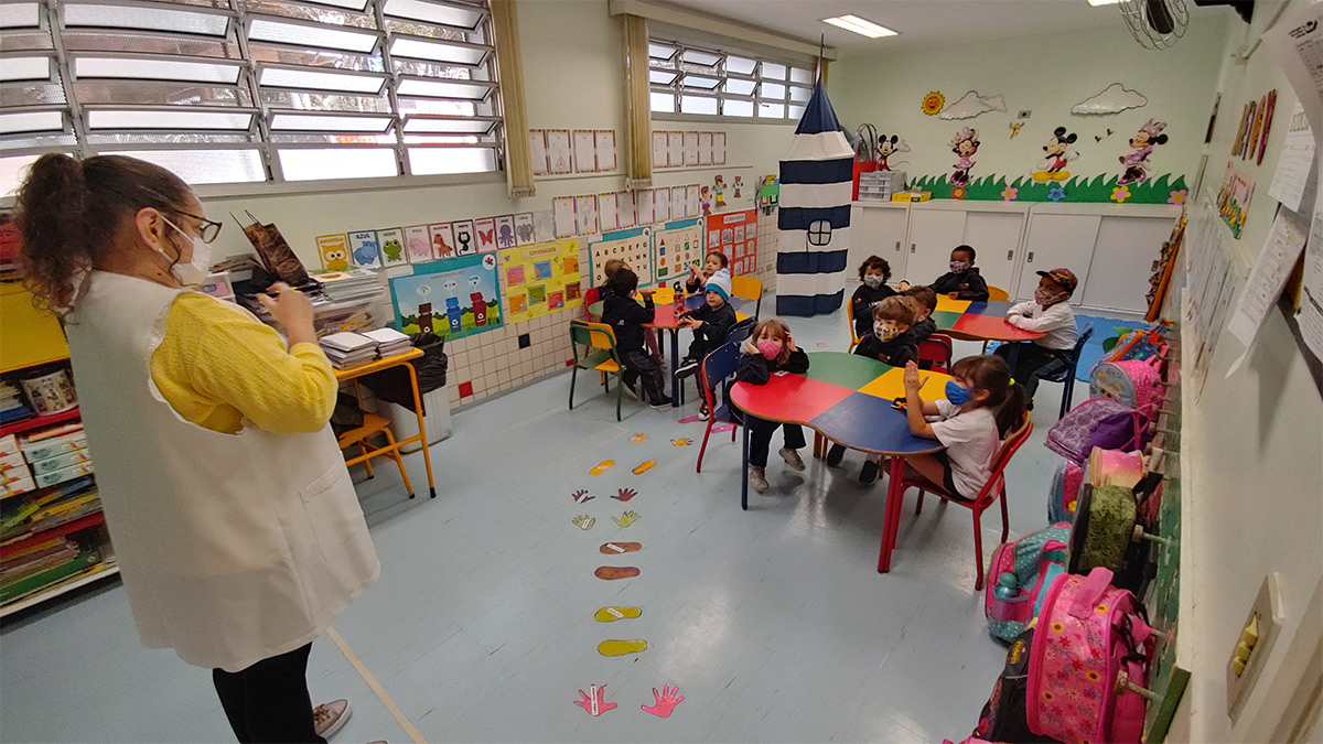 Foto de alunos reunidos em sala de aula observando professora